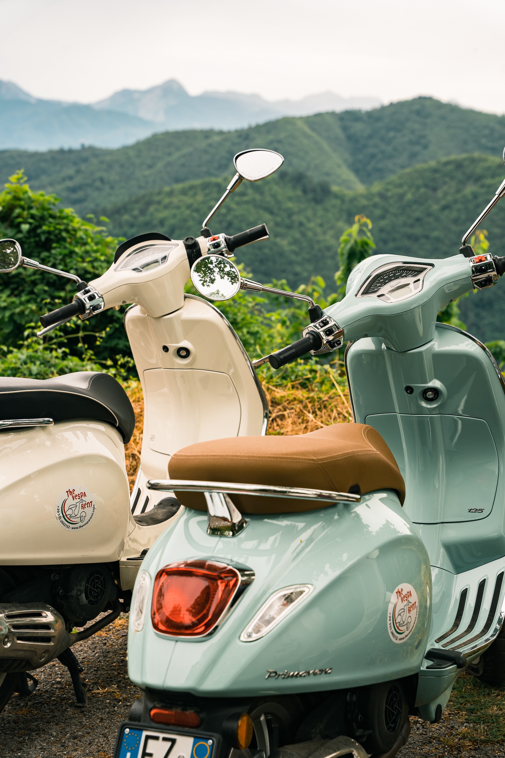 Two Vespa in front of green hills in Italy